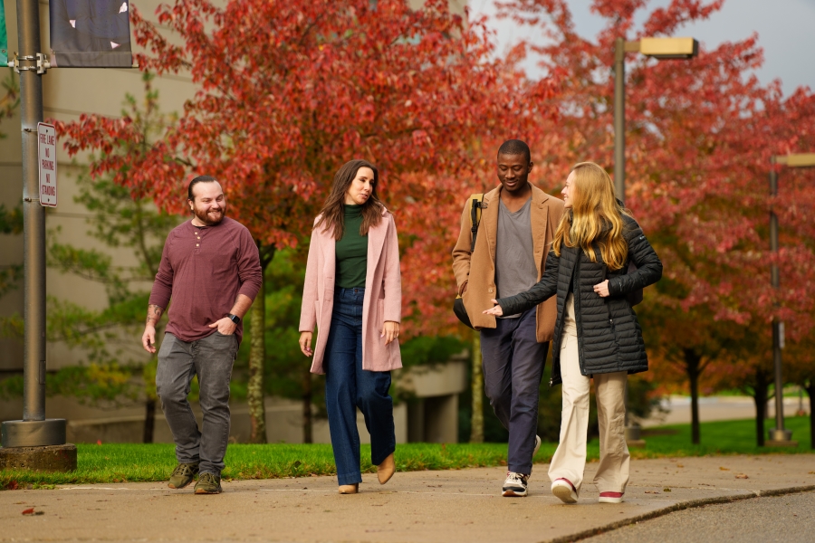 A photo of a group of people walking with Fall foliage behind them.