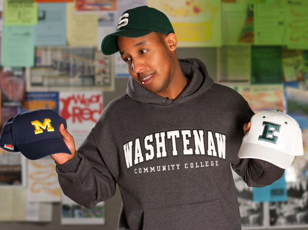Student wearing Washtenaw Community College sweatshirt looking at U of M and EMU hats