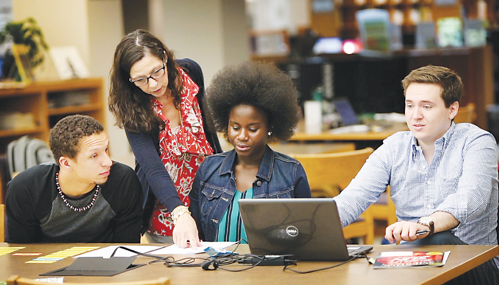 Sandy McCarthy, a librarian at Washtenaw Community College’s Bailey Library, helps STEM Scholars Program participants (from left) Emijoel Lantigua, Araba Gyan and Michael Cooke with a task during one of the program’s summer intensive sessions. | Photo by Kelly Gampel